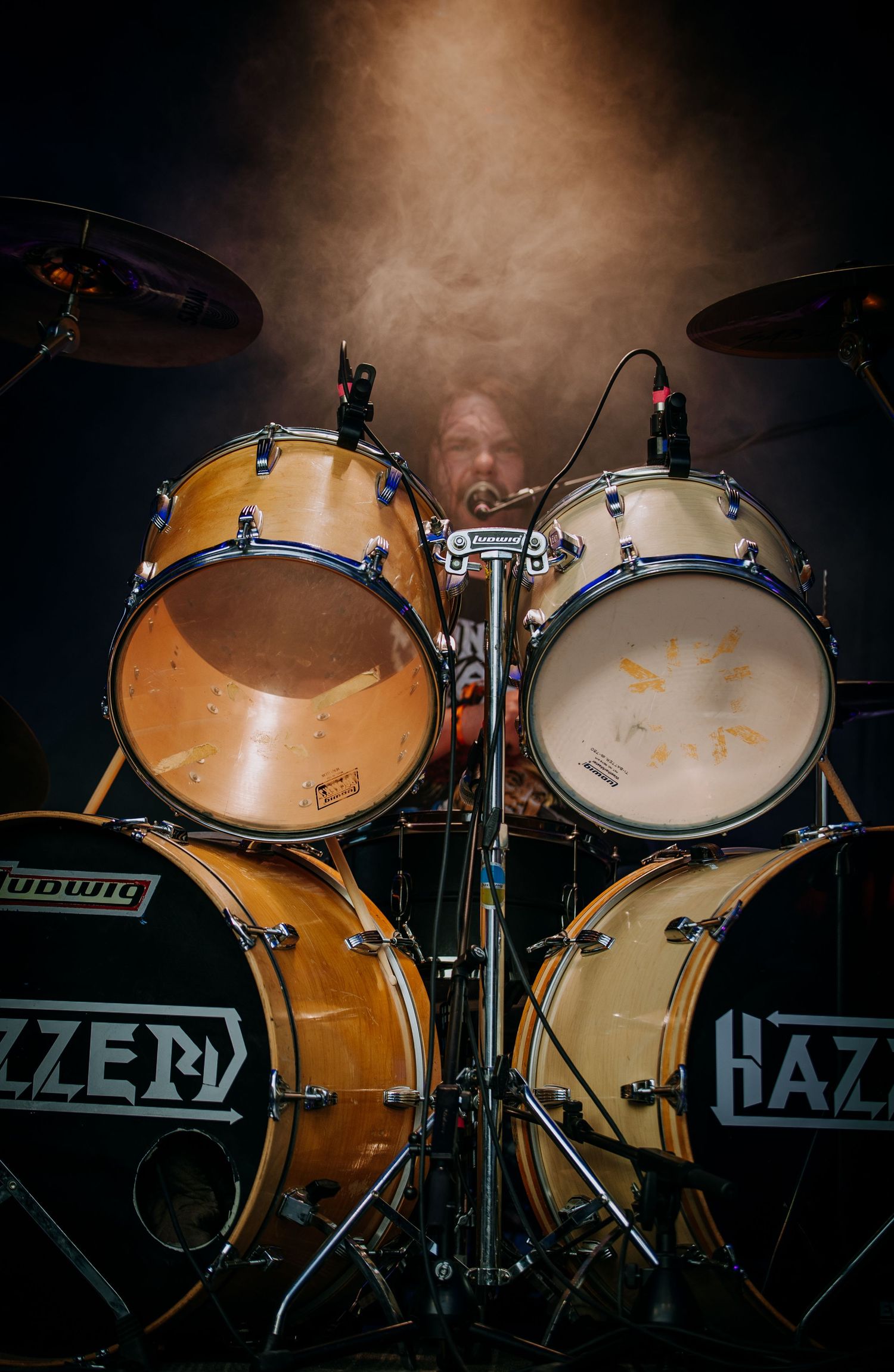 Close-up view of a professional drum kit setup with wooden finish and white cymbals on stage.