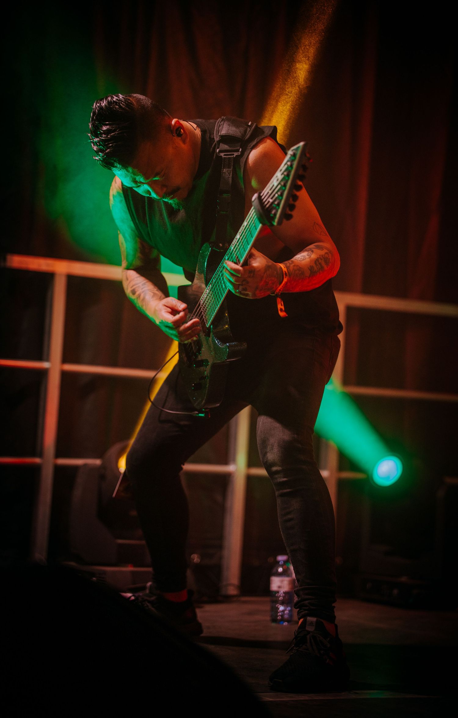 Guitar player performs energetic solo under green stage lighting in dark concert venue.