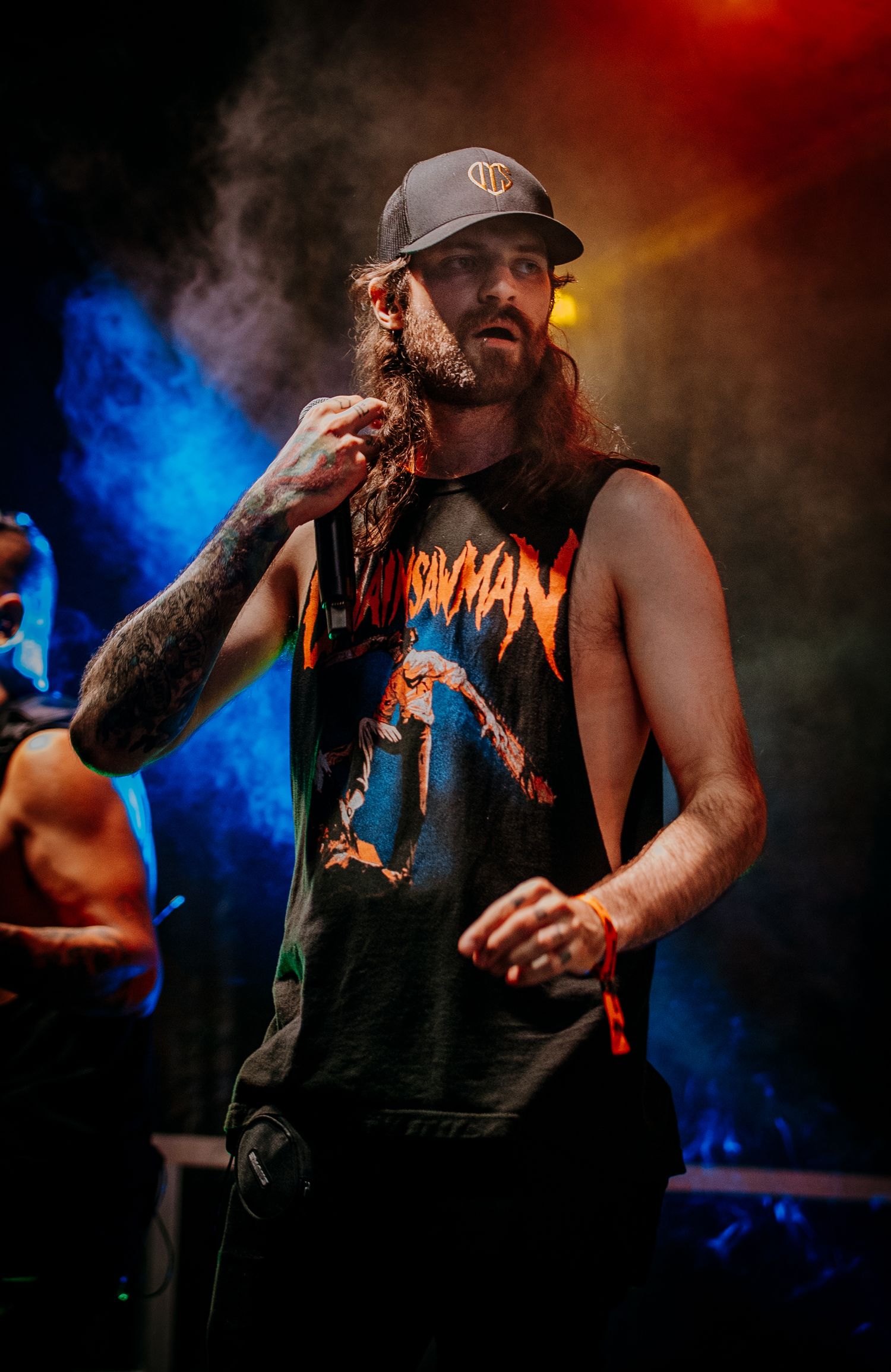 Tattooed musician in black tank top performing passionately against colorful stage lighting.
