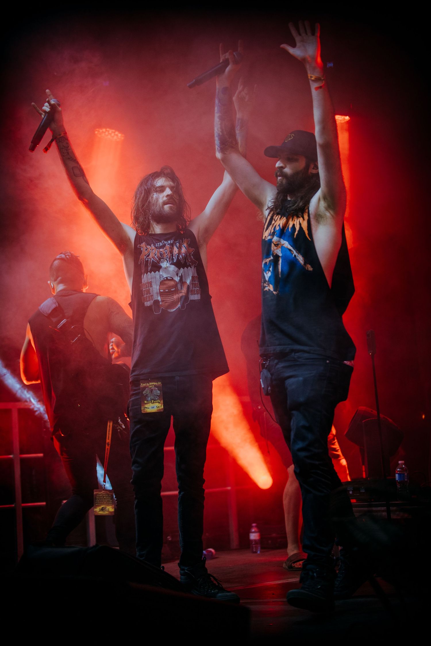 Band members raise their arms triumphantly on stage bathed in red concert lighting during performance finale.