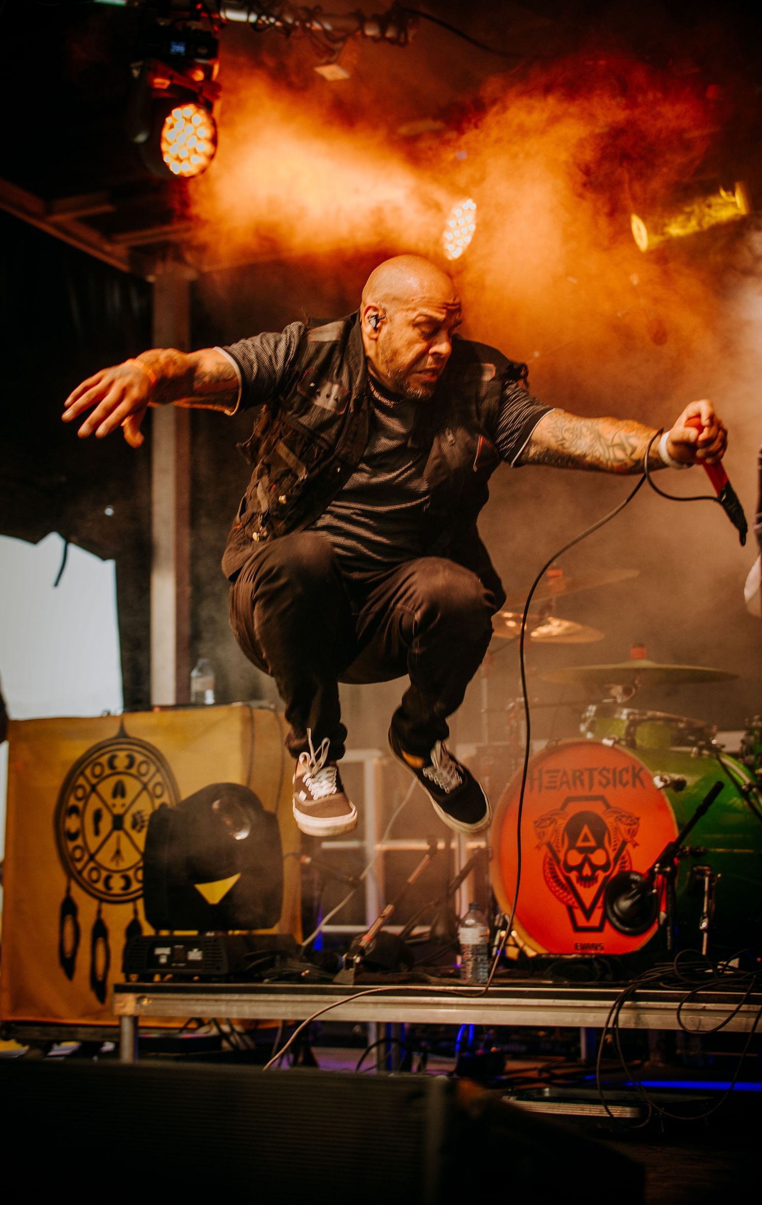 Dynamic performer jumping high on stage surrounded by orange smoke effects and musical equipment.