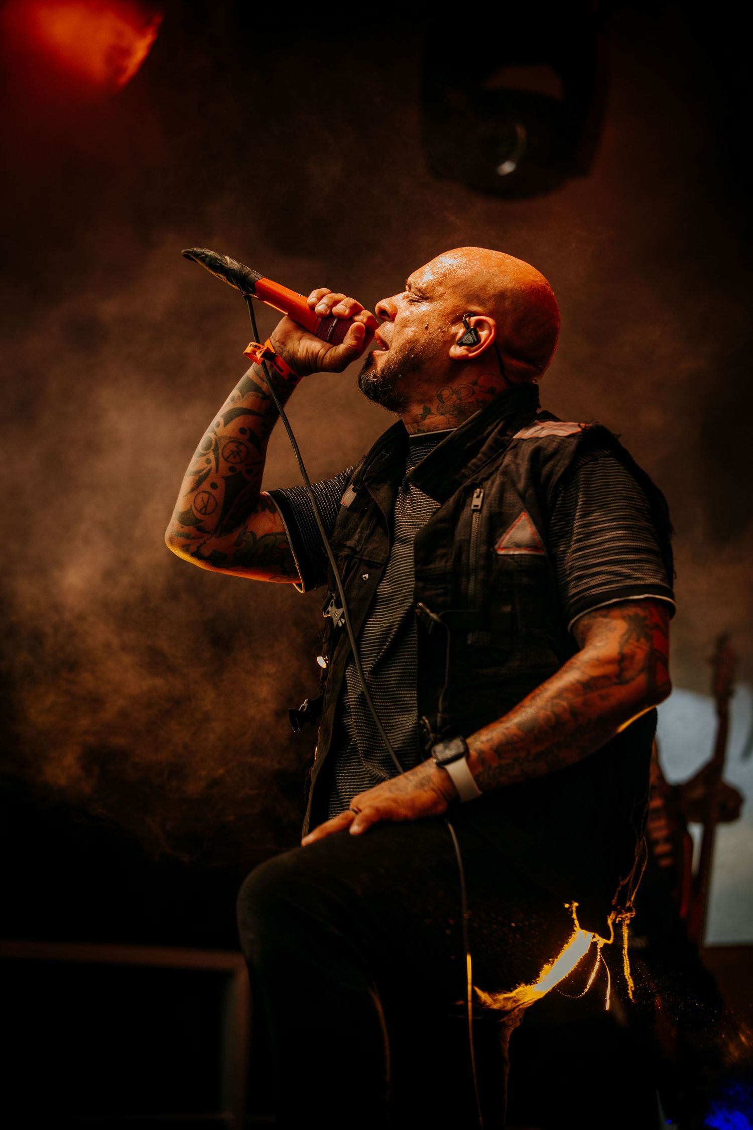 Singer on stage silhouetted against dramatic red lighting and smoke effects during intense performance.