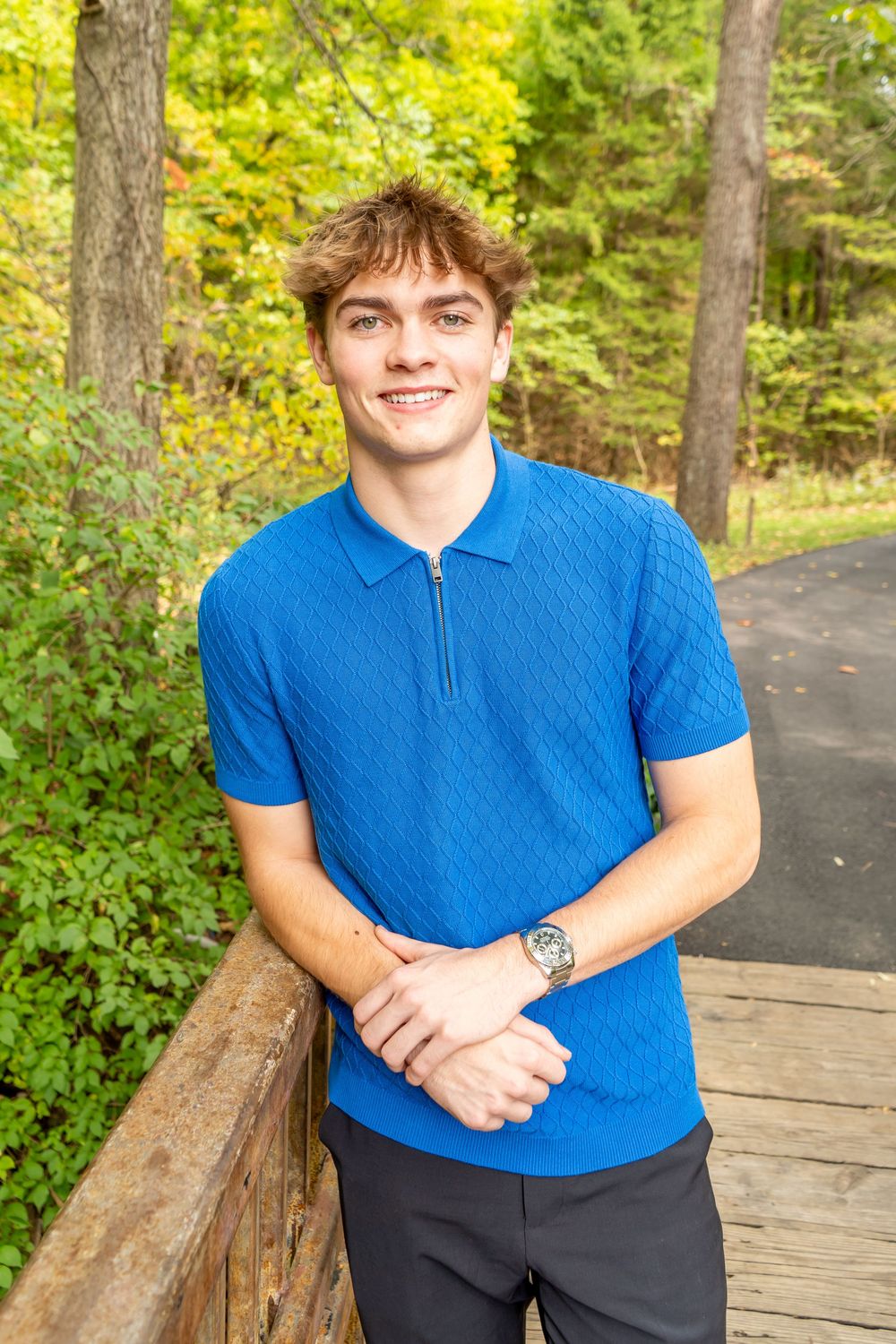 Someone wearing a bright blue polo shirt poses on a wooden deck surrounded by lush green forest scenery.