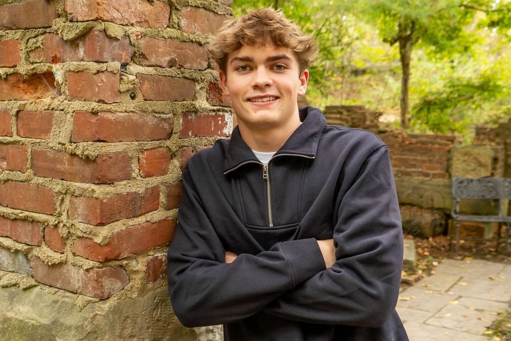 An outdoor casual portrait photos showing someone against brick walls and greenery in a quarter-zip sweater.
