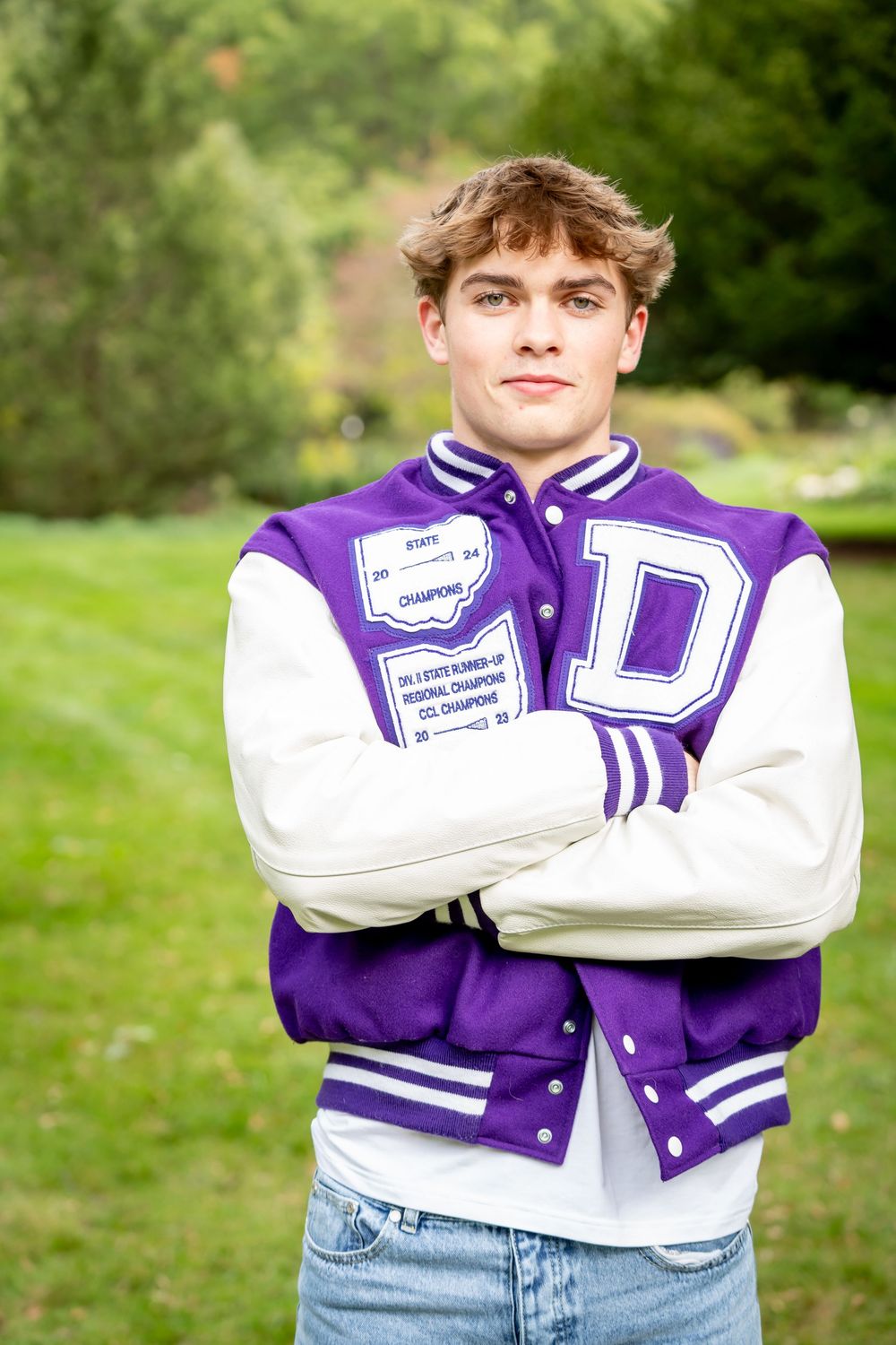 Purple and white varsity letter jacket shown in multiple poses against green outdoor background.