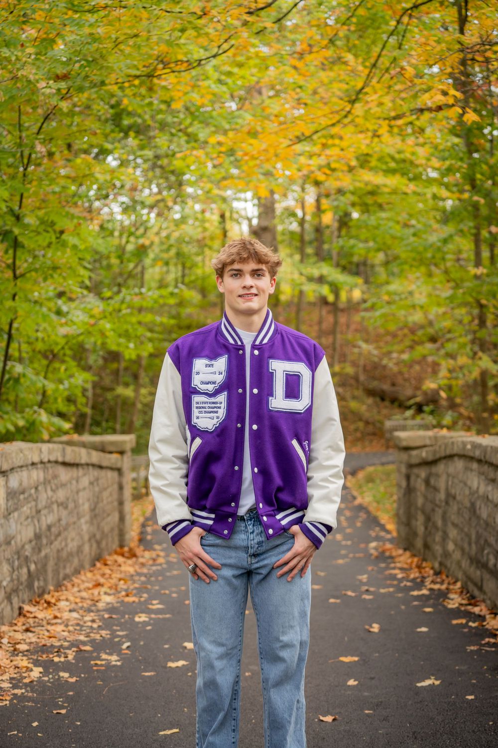 Autumn scene along stone-walled walkway with vibrant yellow leaves overhead and purple varsity jacket in view.
