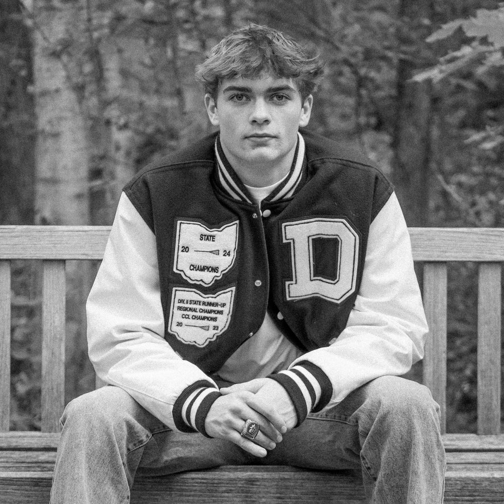 Black and white cropped portrait photograph showing person sitting on wooden bench outdoors.