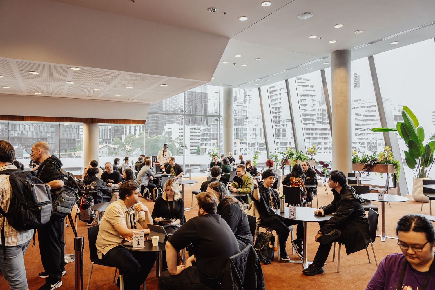 Modern open office space features long communal tables and large windows overlooking a city skyline.