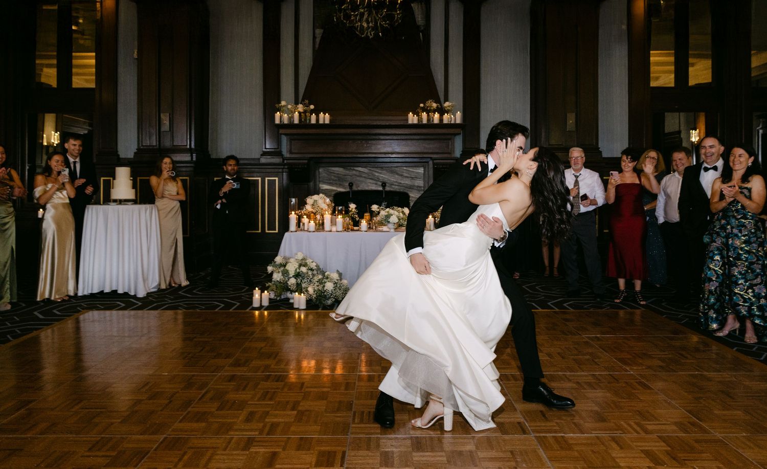 A couple in formal attire glides gracefully across a wooden dance floor during a wedding celebration.