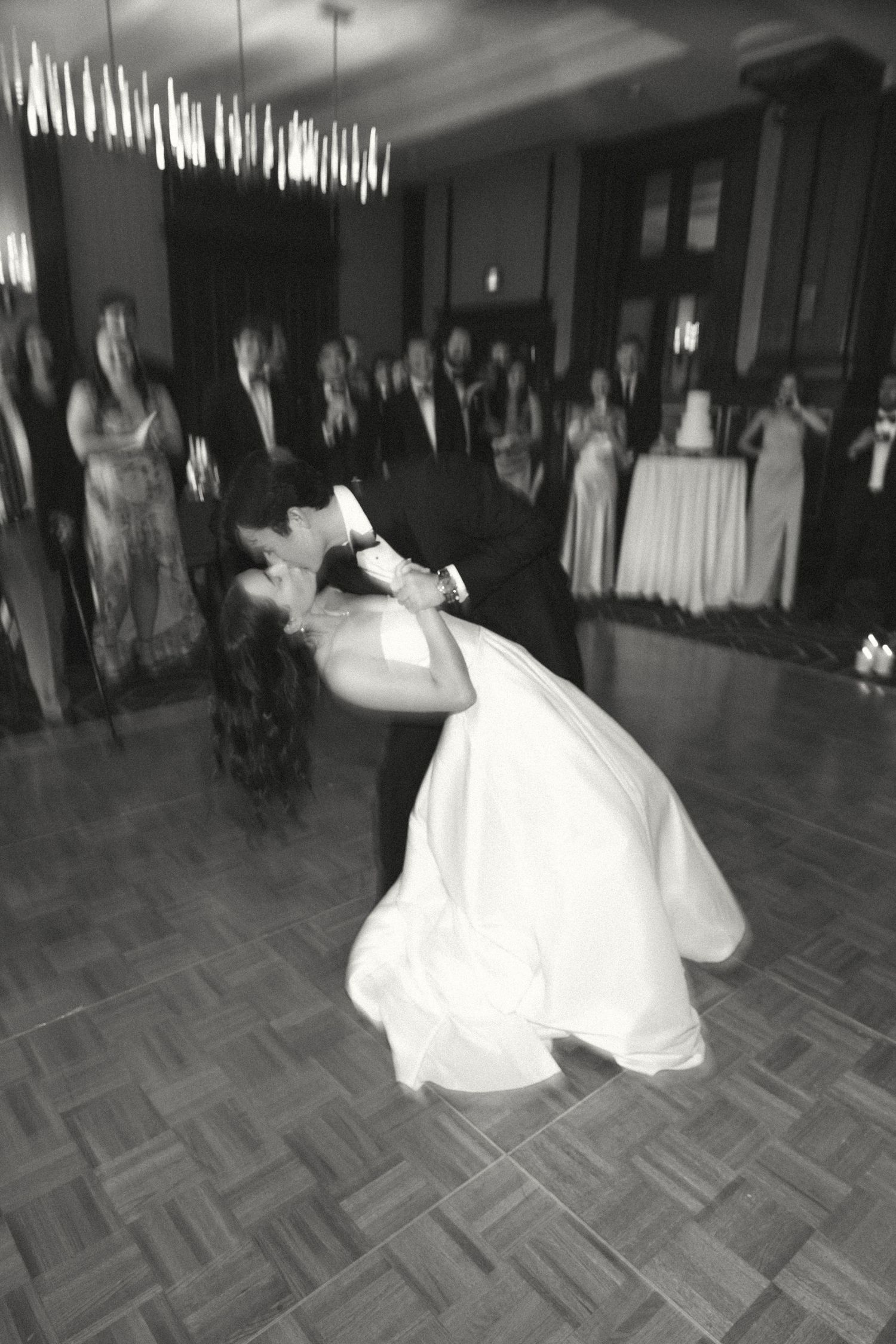 A dramatic black and white photo of a wedding dance with a bride in a flowing white dress dipping on the dance floor.