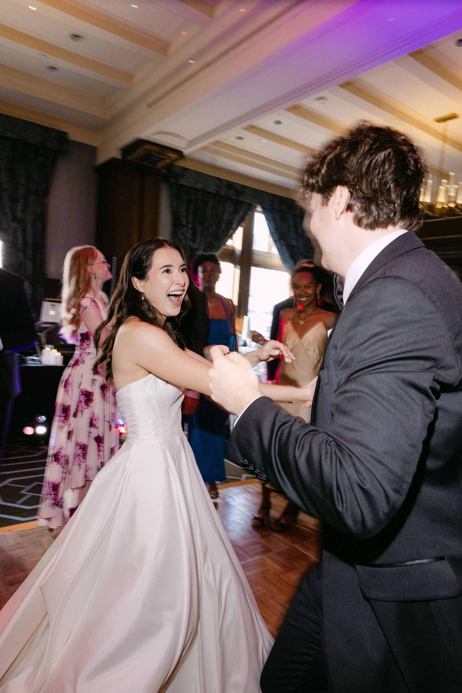 A joyful wedding dance moment with guests in the background and purple lighting overhead.