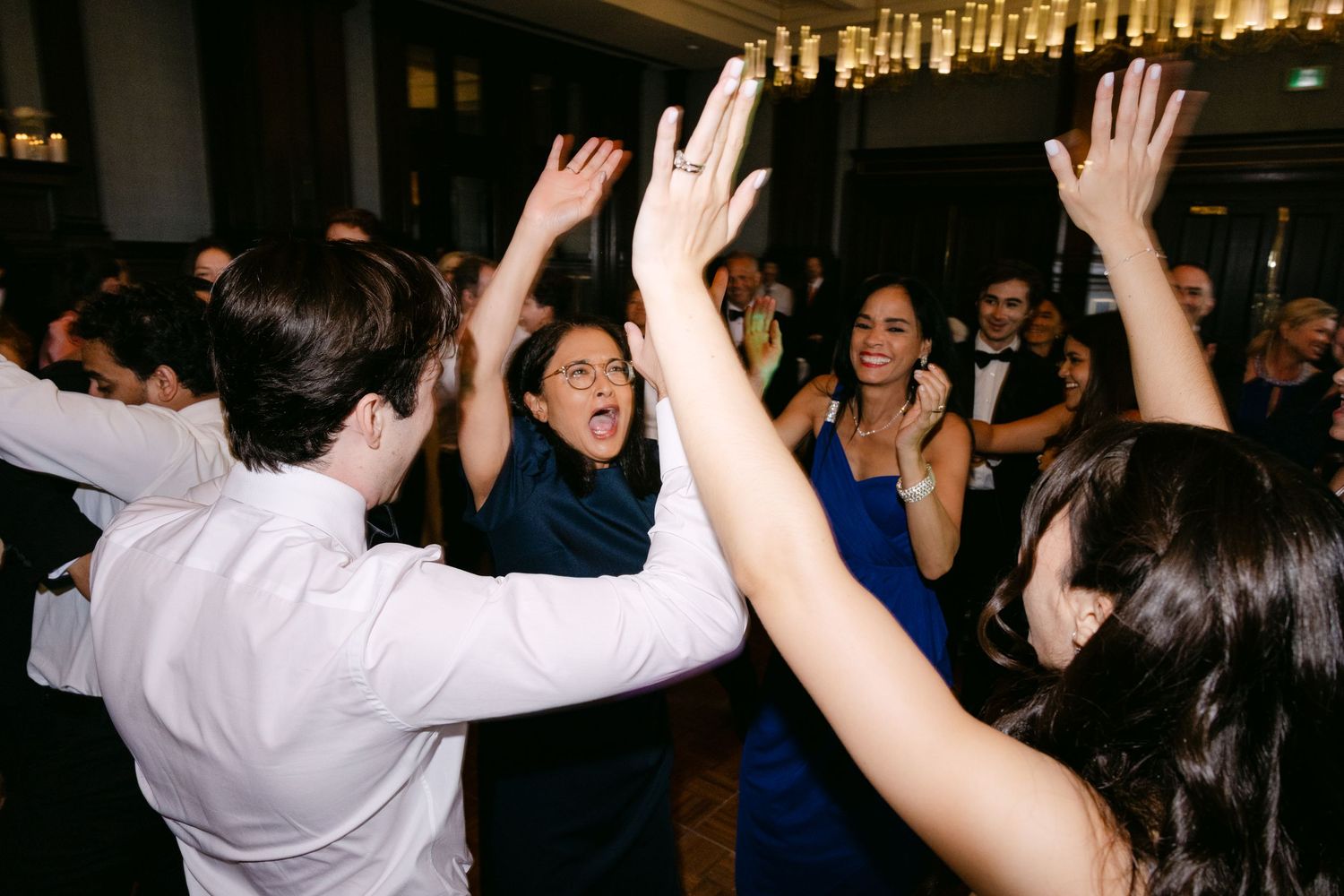 Large crowd of people dancing and celebrating with raised hands at a lively indoor party or celebration event.