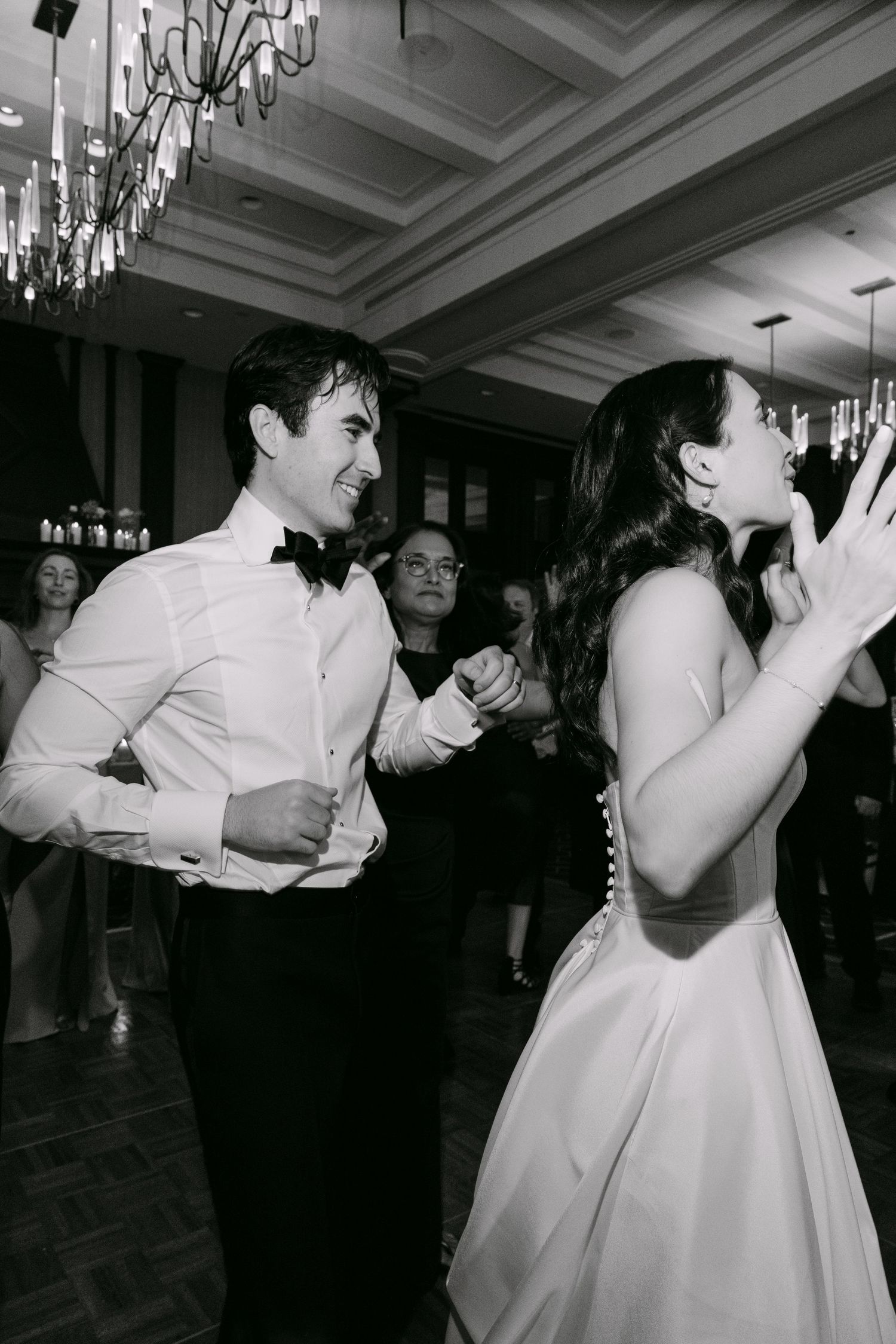 A couple dances enthusiastically at a wedding reception under elegant chandeliers.