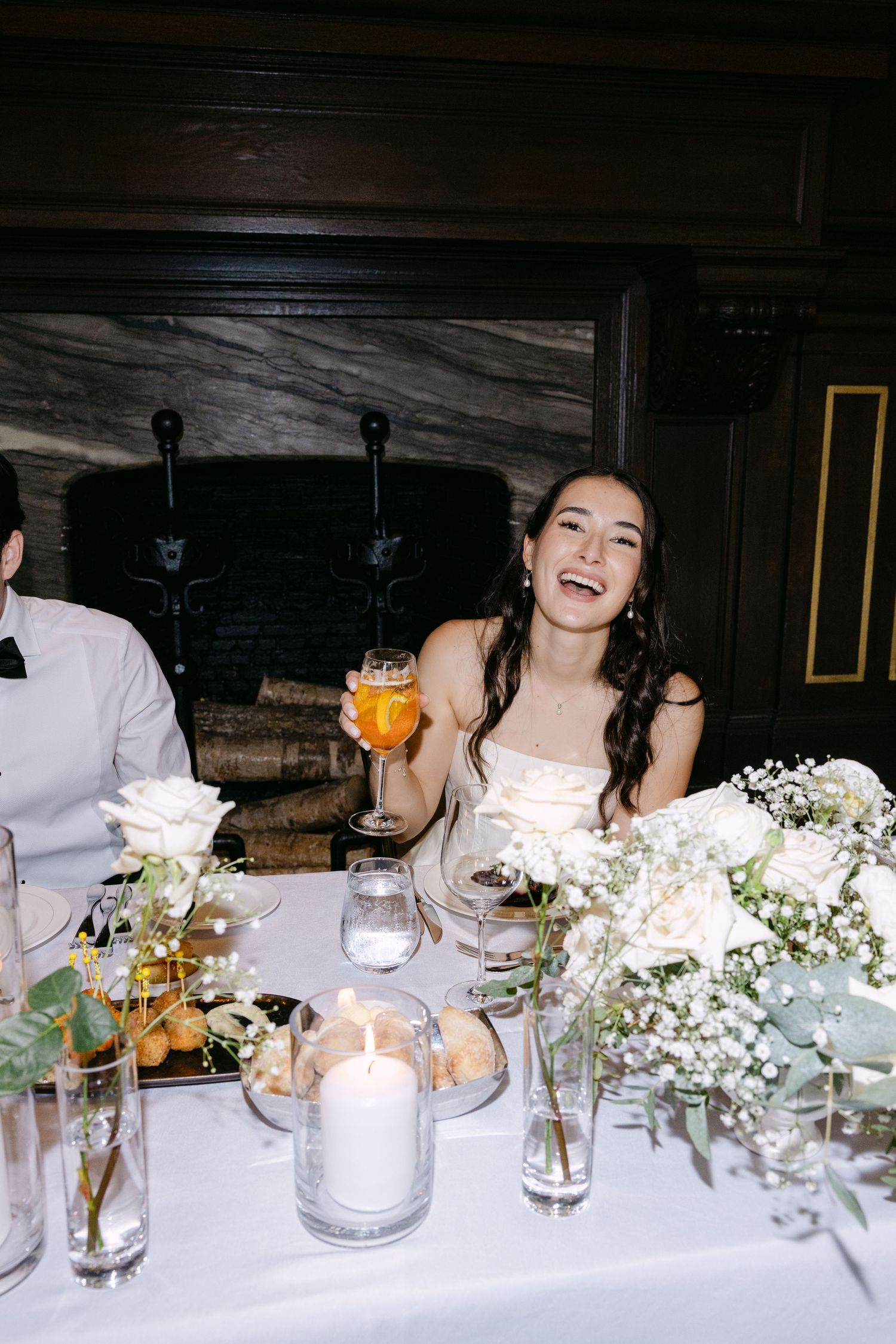 A wedding guest enjoys a drink at an elegantly decorated reception table with white flowers and candles.