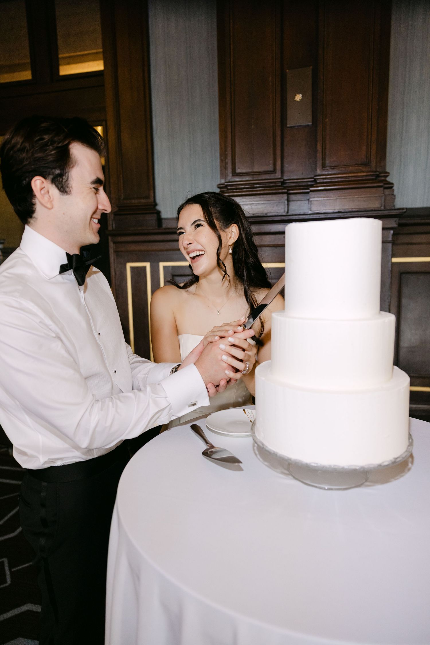 A sweet moment of cutting the classic white three-tier wedding cake together.
