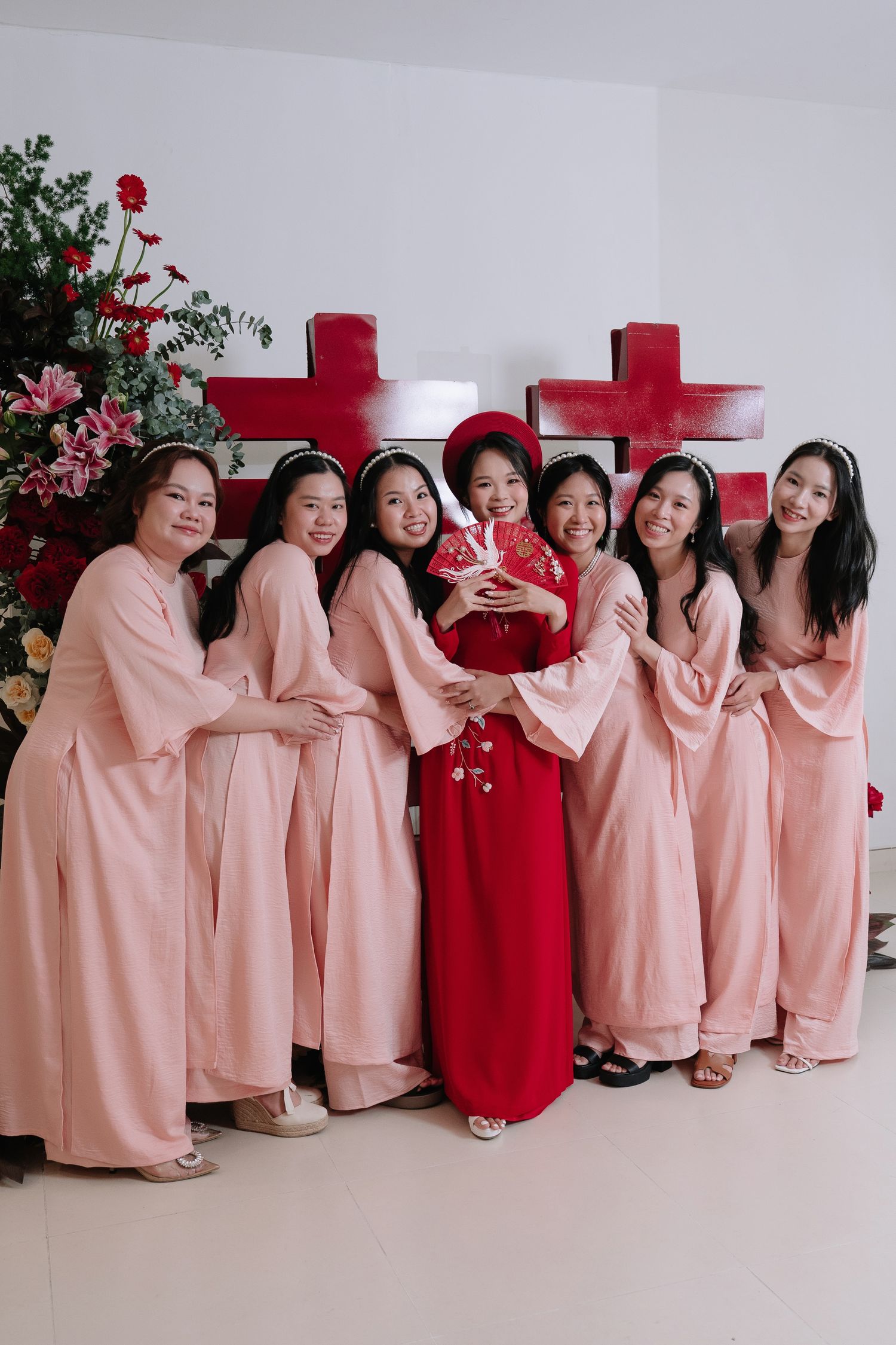 Vietnamese bride in red ao dai poses with six bridesmaids in pink ao dai at wedding celebration.