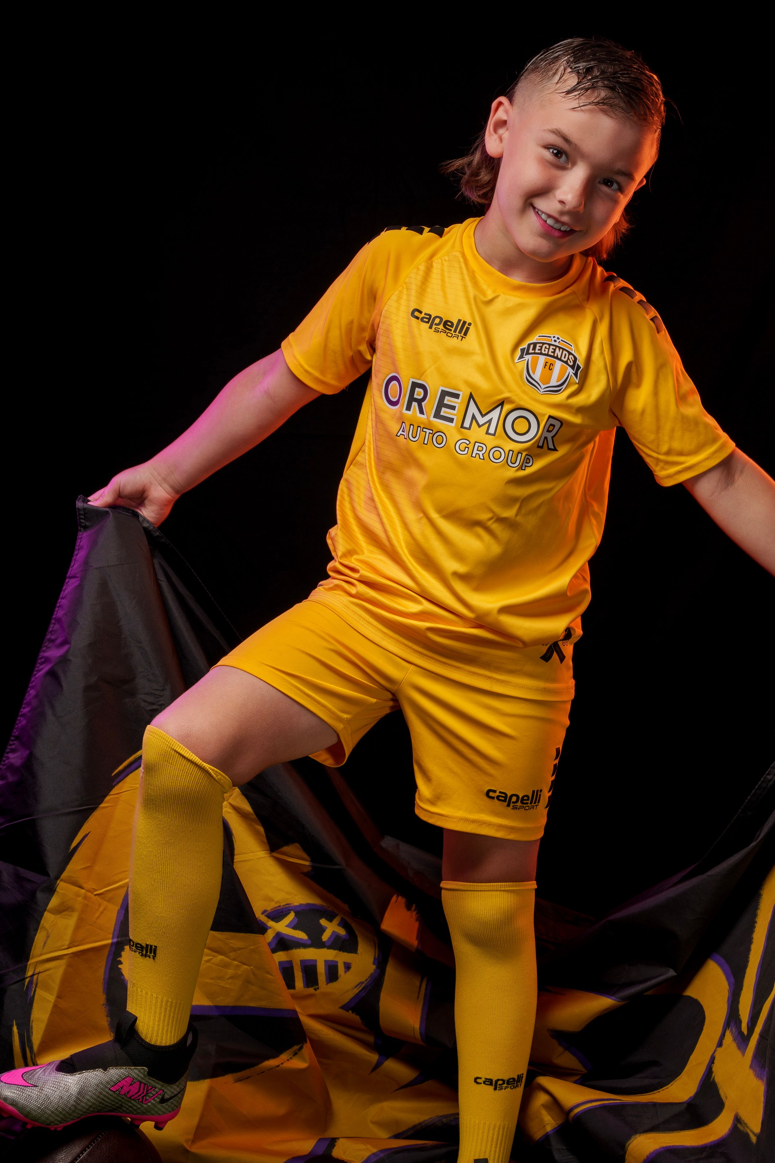 Athlete in yellow Legends FC uniform strikes playful poses with football in studio setting.