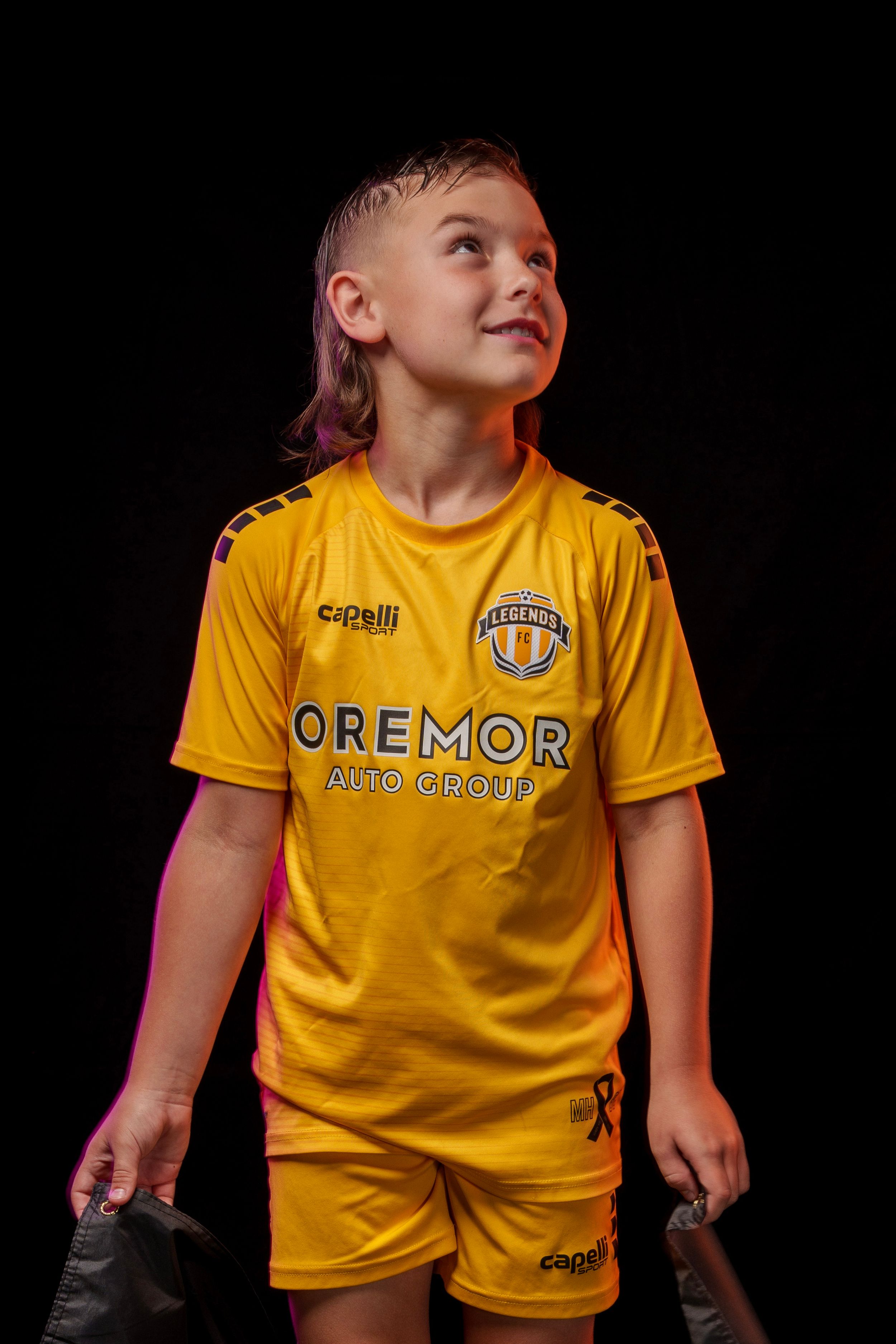 Young athlete poses in bright yellow Legends FC soccer uniform against black background.