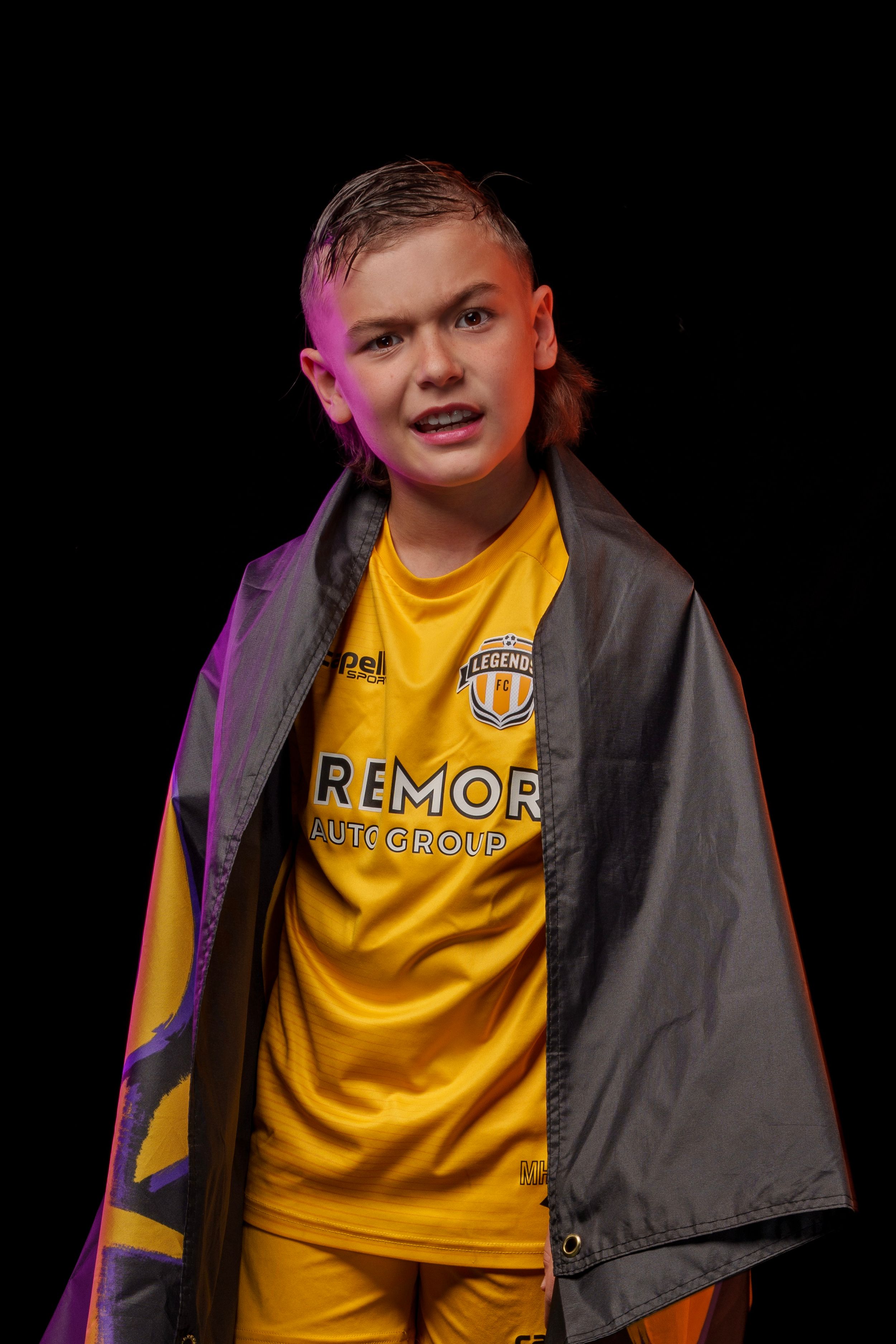 Soccer player wearing yellow Legends FC jersey and grey cape poses in dramatic lighting.