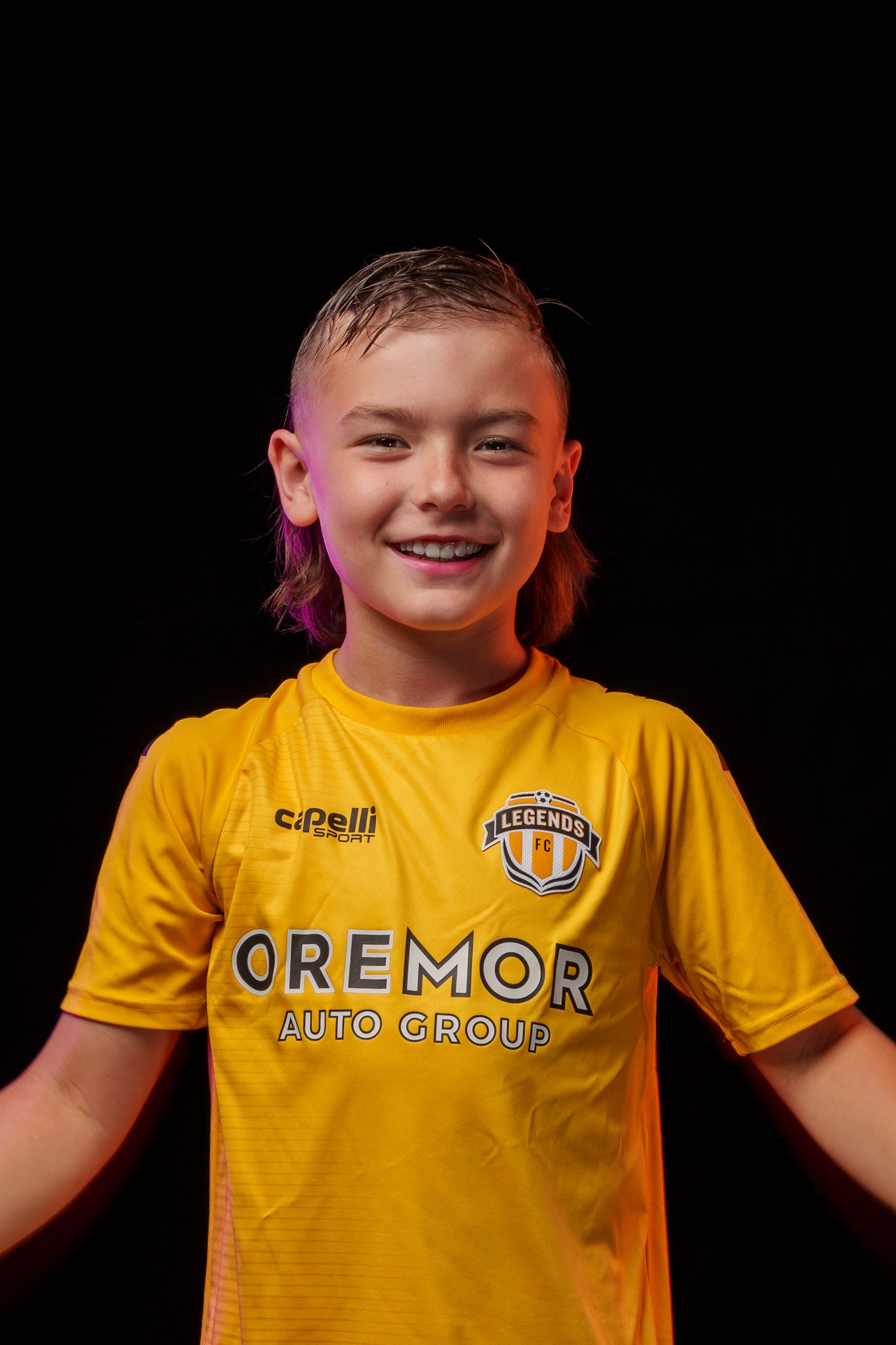 Young athlete in bright yellow Legends FC soccer uniform on black background.