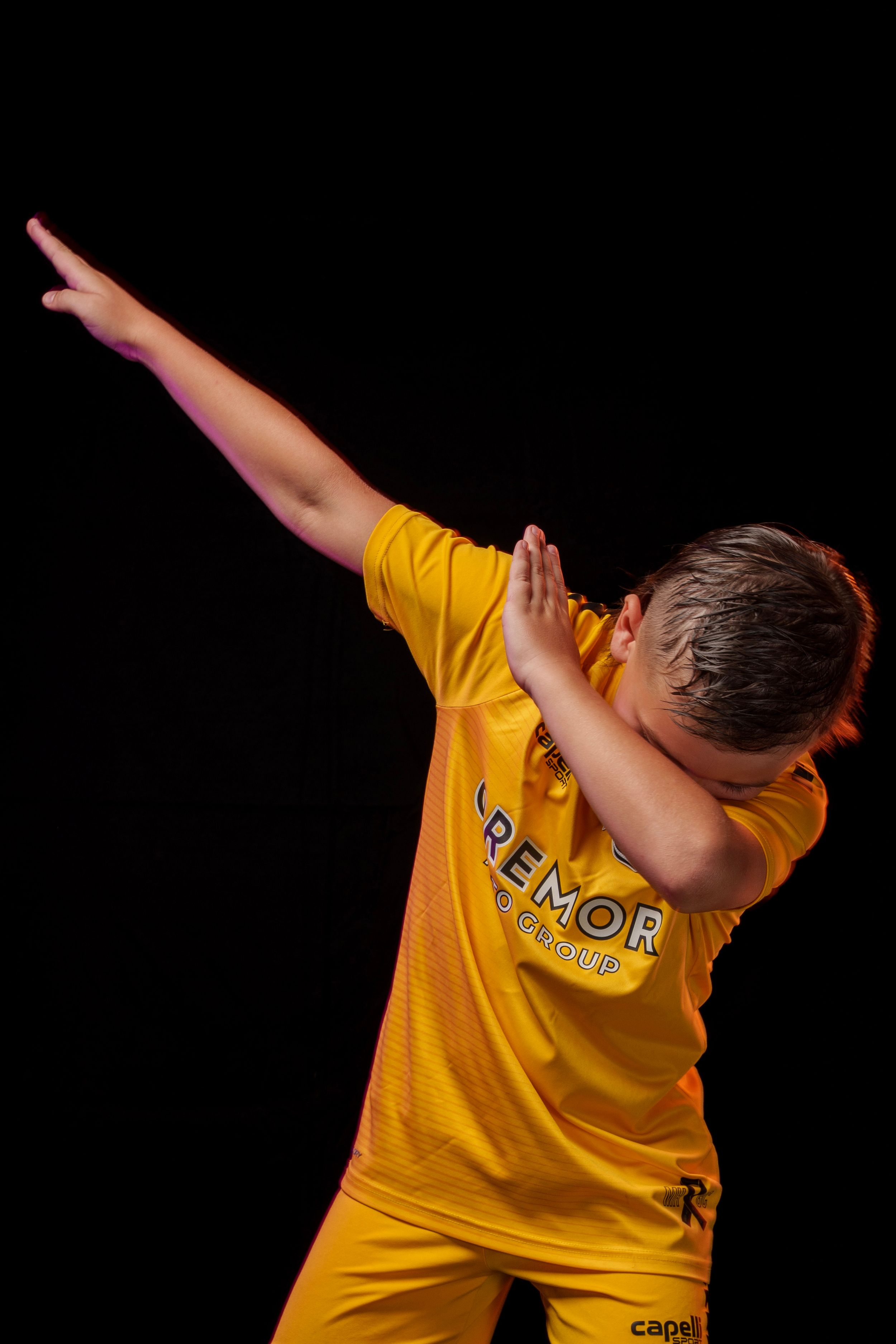 Soccer player in yellow jersey performs dabbing dance move in studio setting.