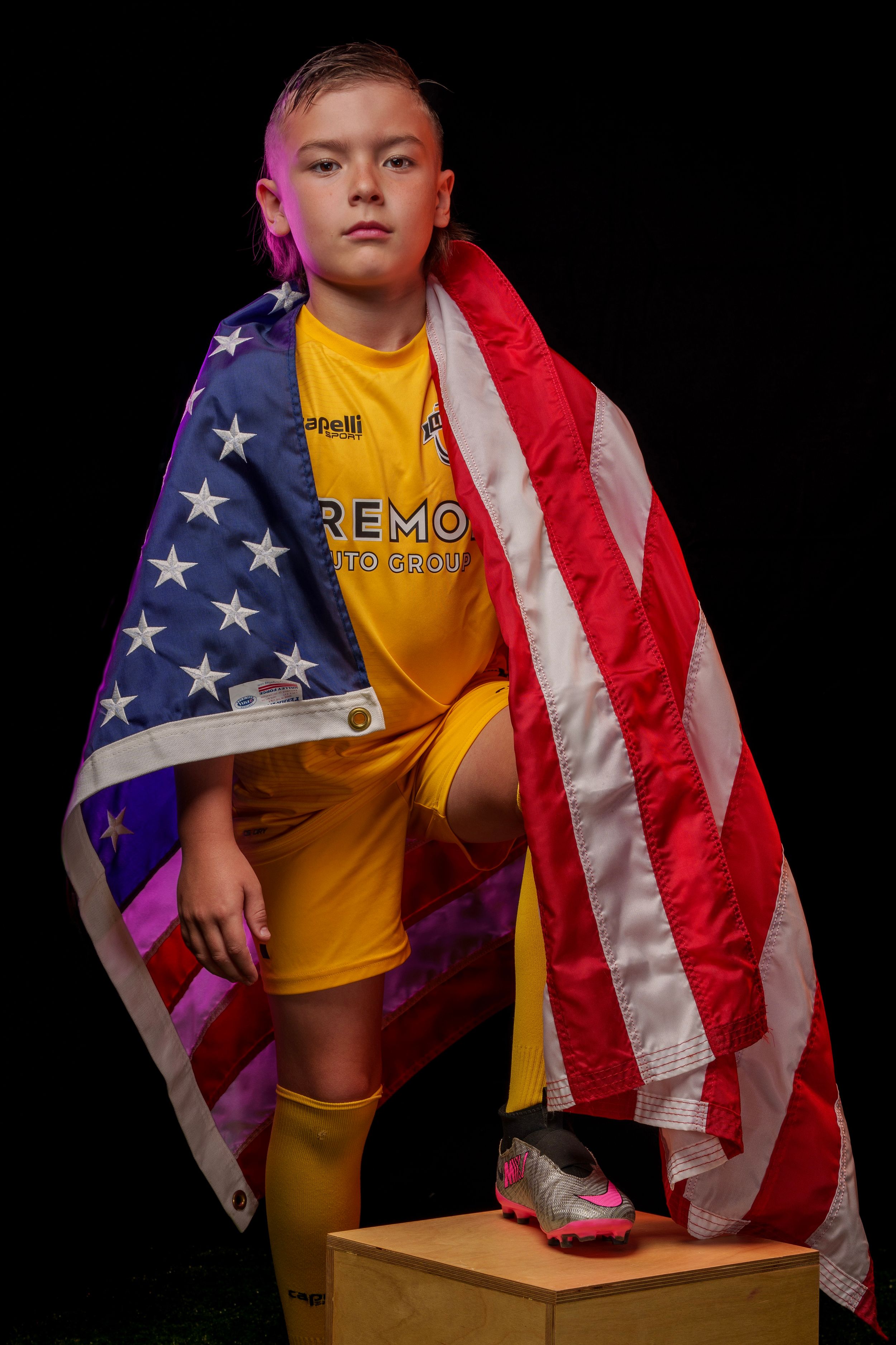 Person in yellow sports uniform stands confidently with American flag draped around shoulders.