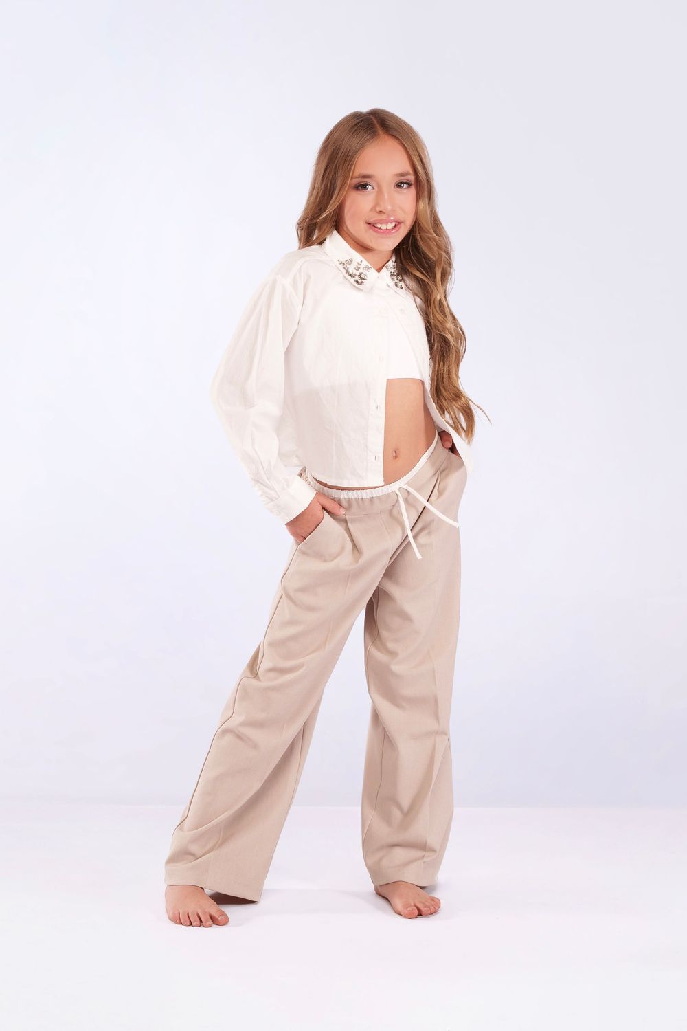 Dancer in white top and beige pants performs playful poses in studio setting.