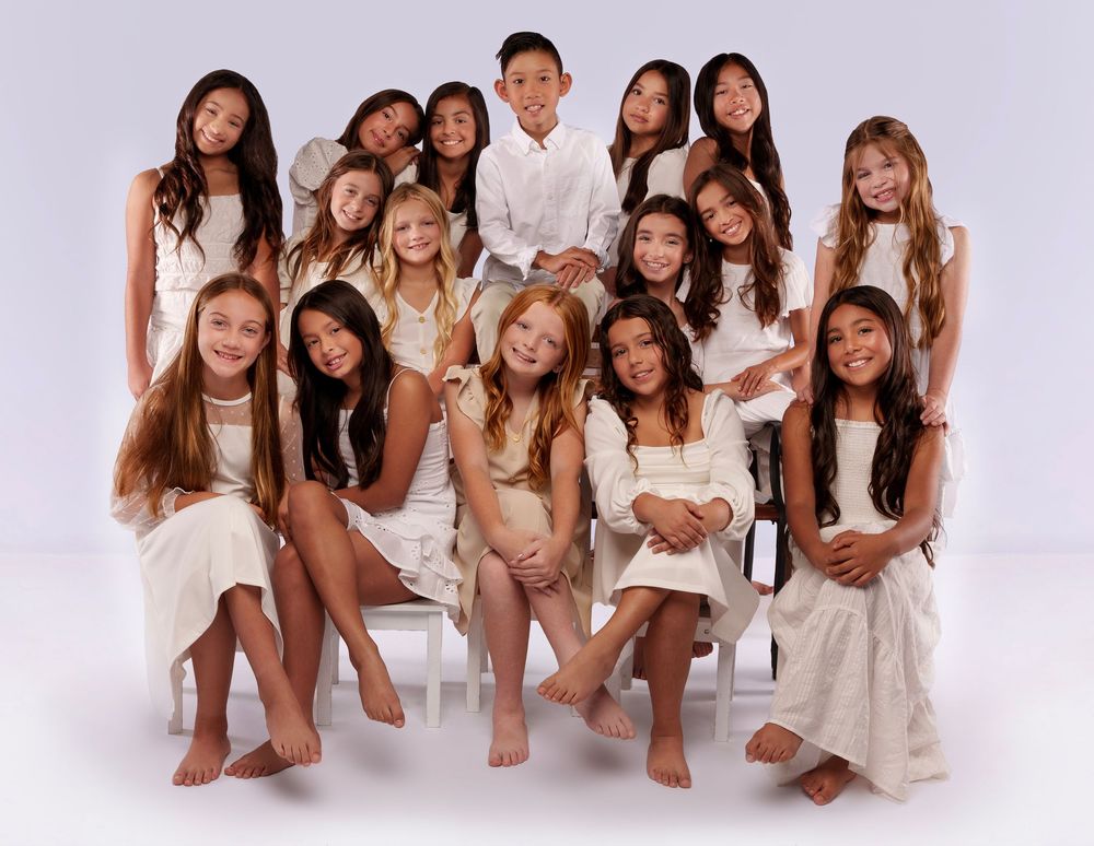 Group portrait of young dancers wearing white outfits posing together in studio setting.