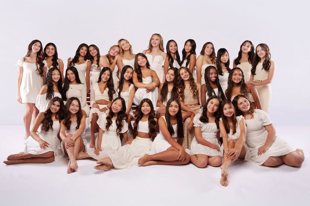 Studio portrait of women's group wearing coordinated white outfits in artistic formation.