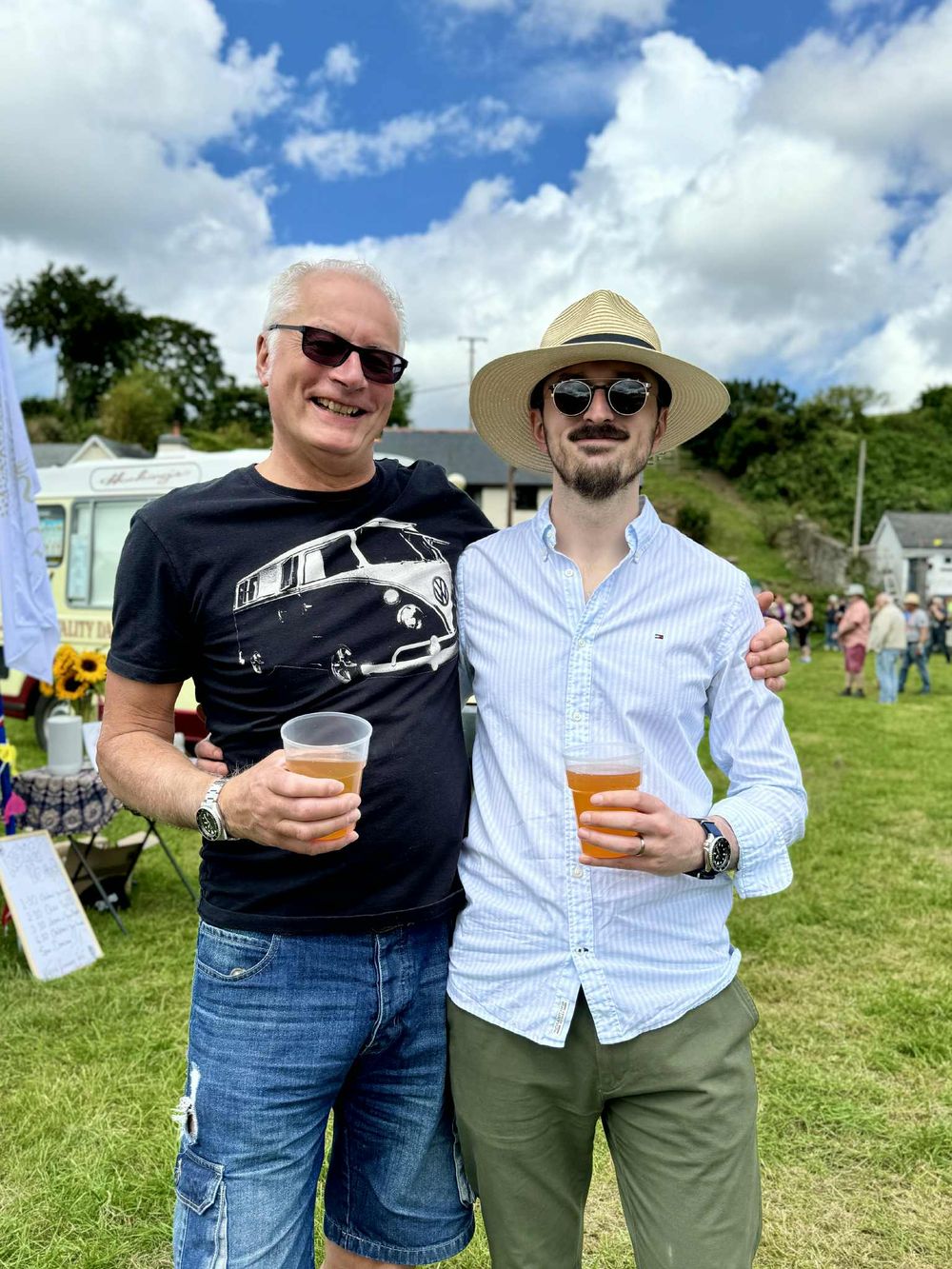 Two people enjoying drinks and conversation together at an outdoor summer festival on a grassy field.