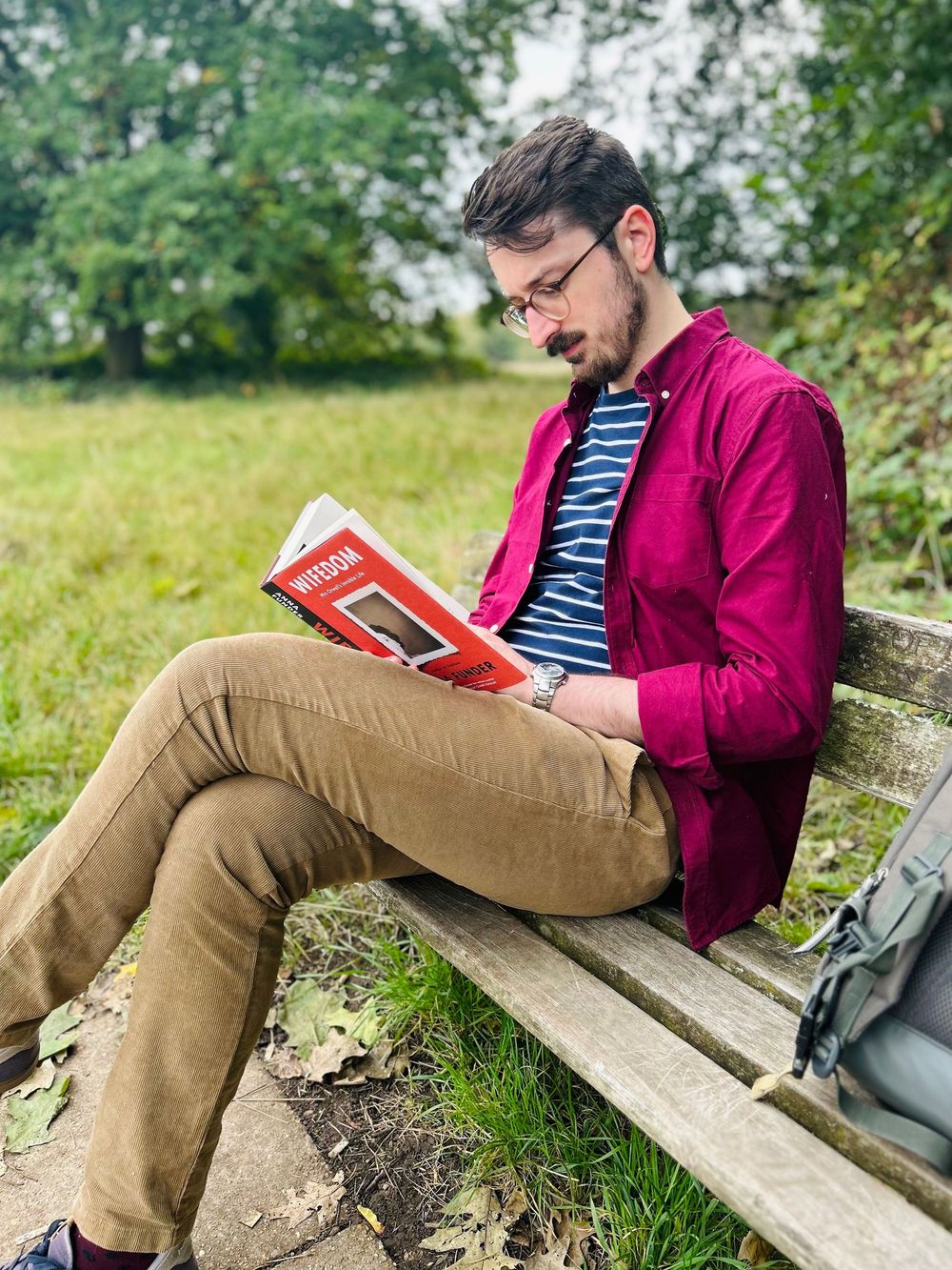 Person in pink sweater reading book while relaxing on wooden bench in nature.