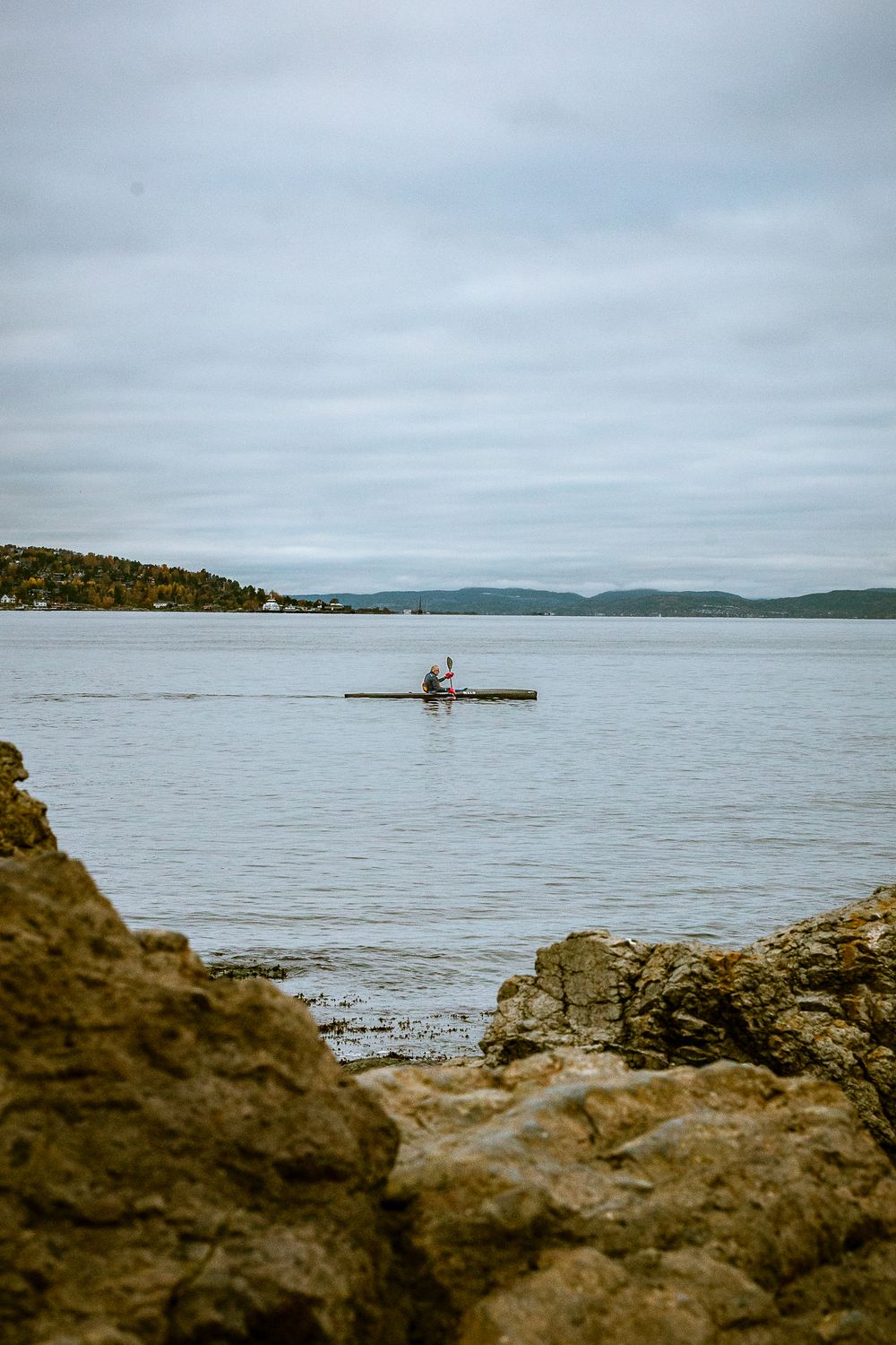 Rocky coastline with calm water and distant islands under overcast sky.
