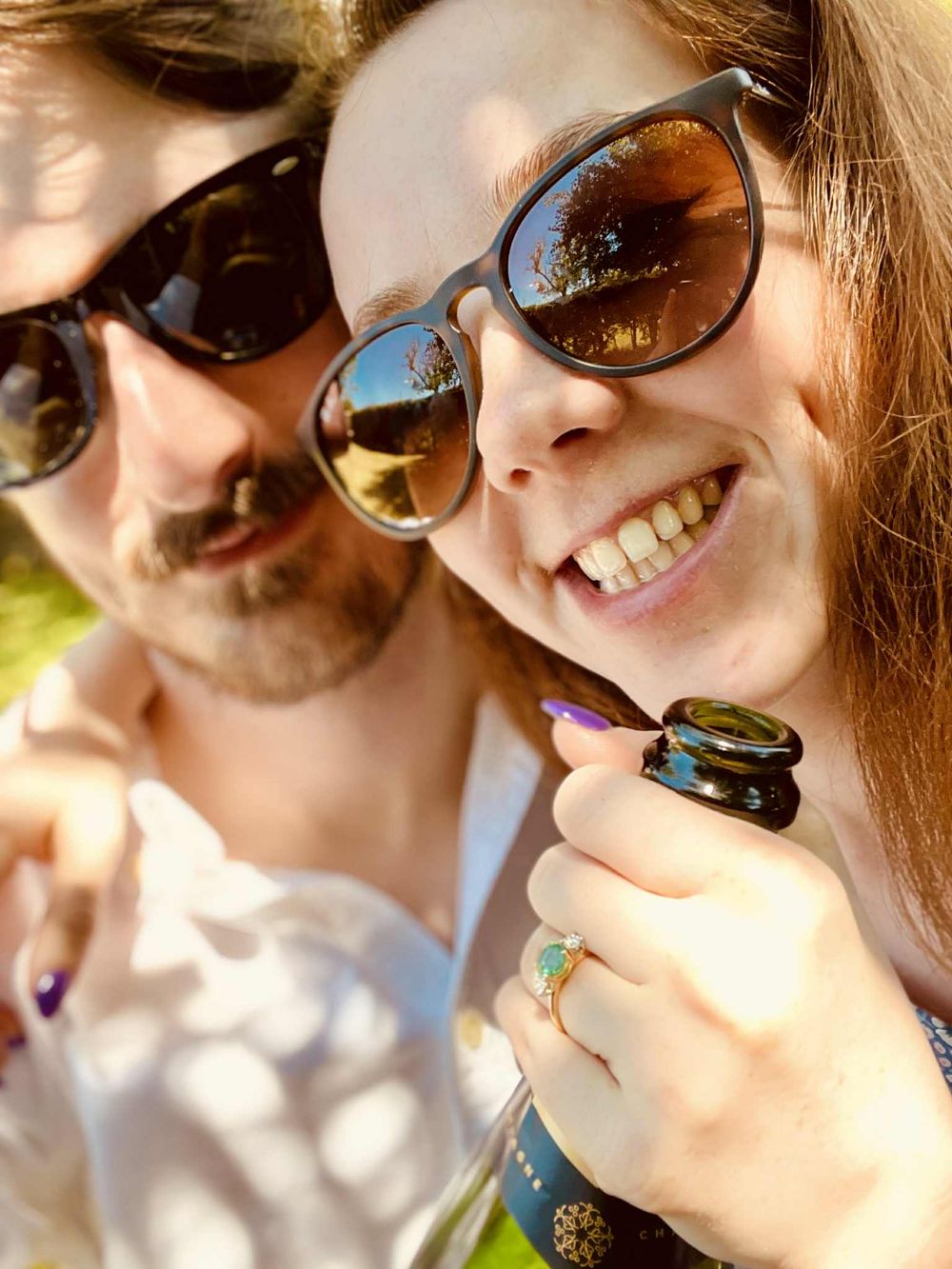 Couple wearing sunglasses share intimate outdoor selfie moments in bright sunlight.