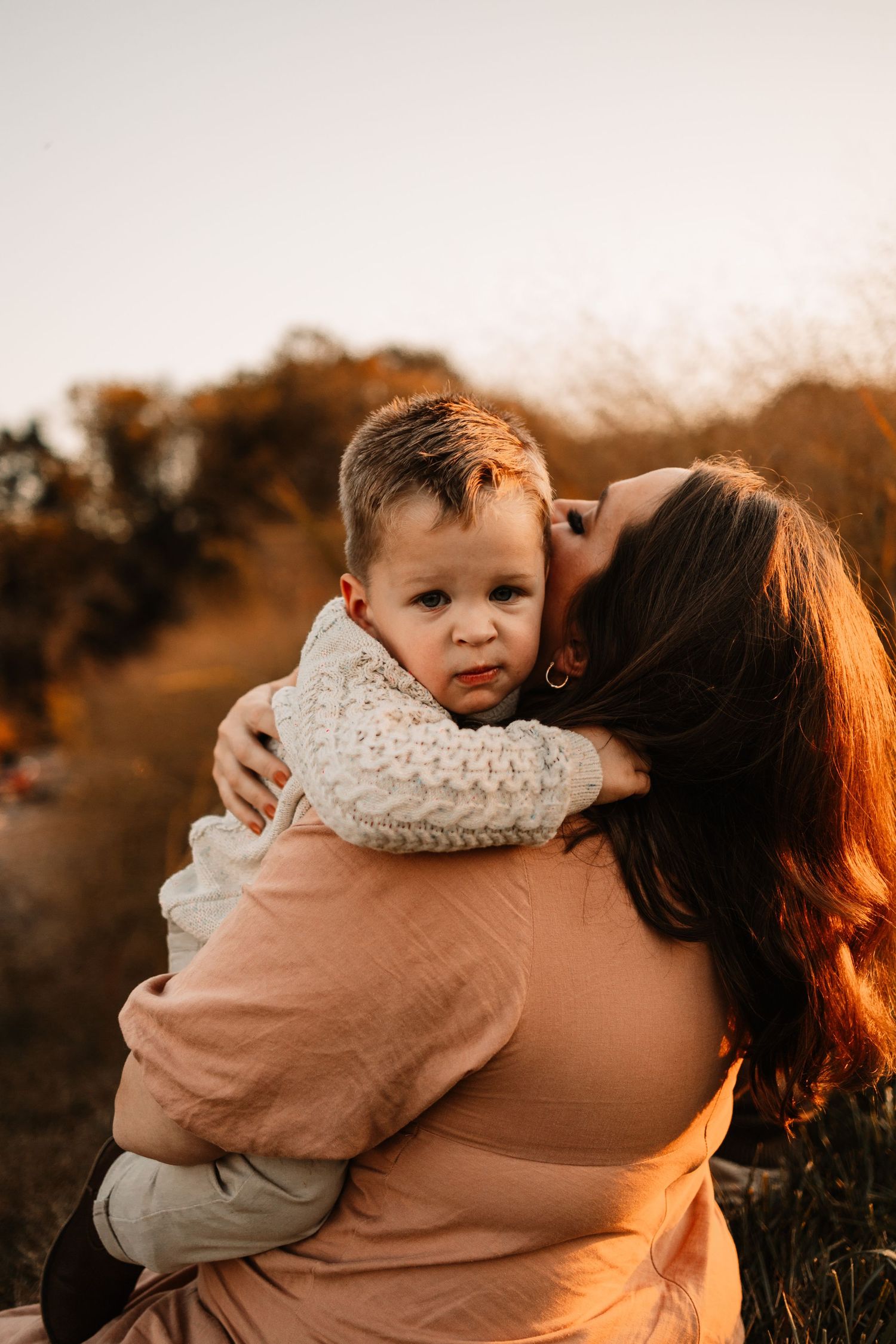 Pregnant mother embracing toddler son in warm sunset light during fall outdoor maternity session.