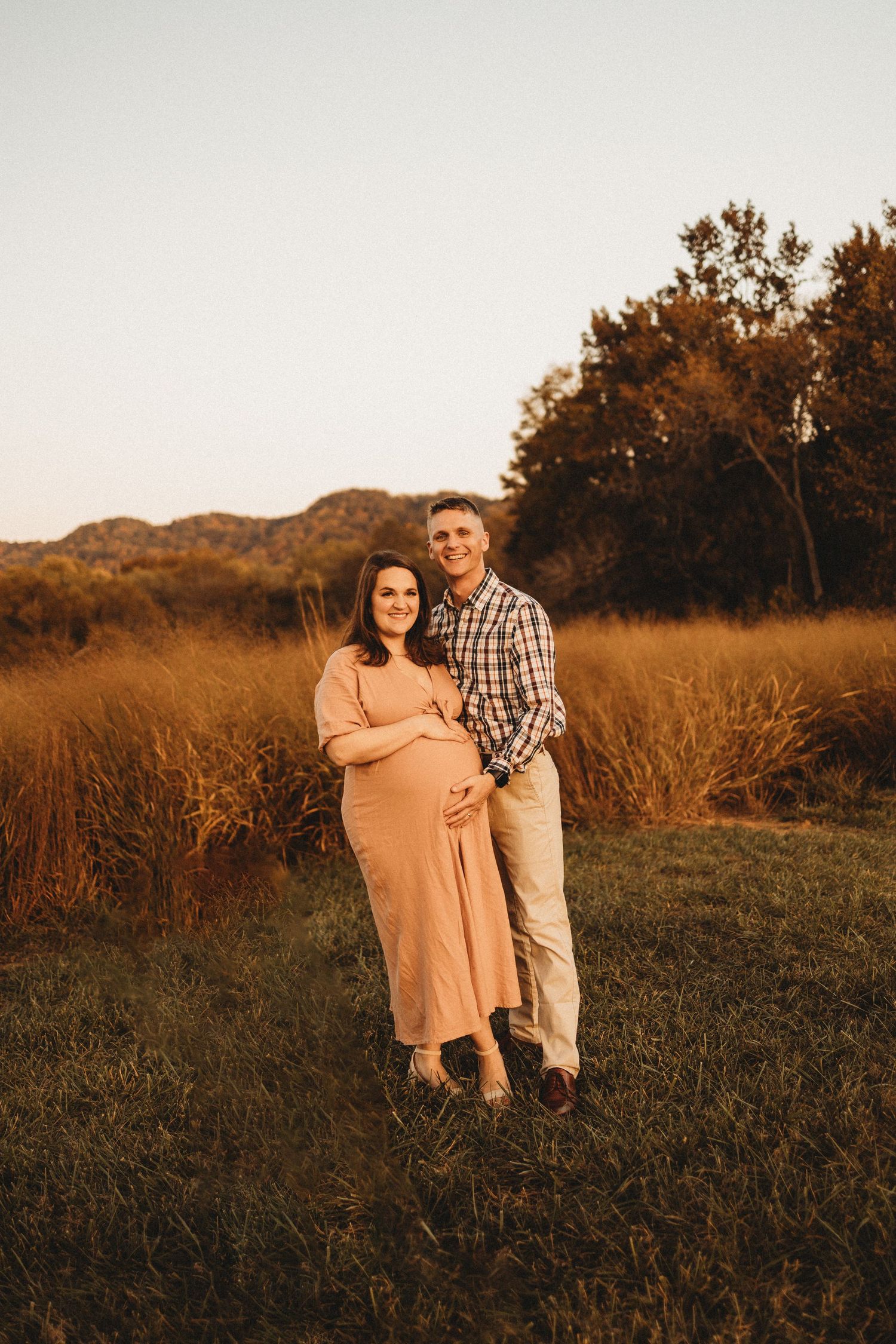 Couple posing together in fall field at sunset during outdoor maternity photography session.