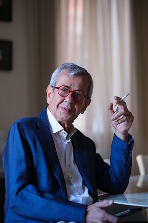Senior businessman in blue suit jacket holding cigarette in contemplative pose.