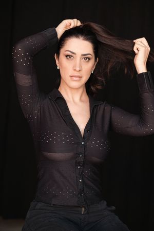 Fashion portrait in sheer black studded button-up shirt against dark background.