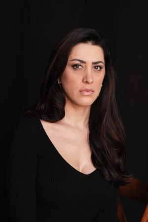Moody portraits against black background wearing dark v-neck top.