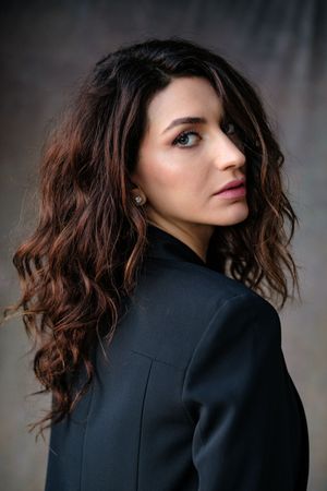 Dramatic portrait series in black blazer with tousled wavy hair against dark background.