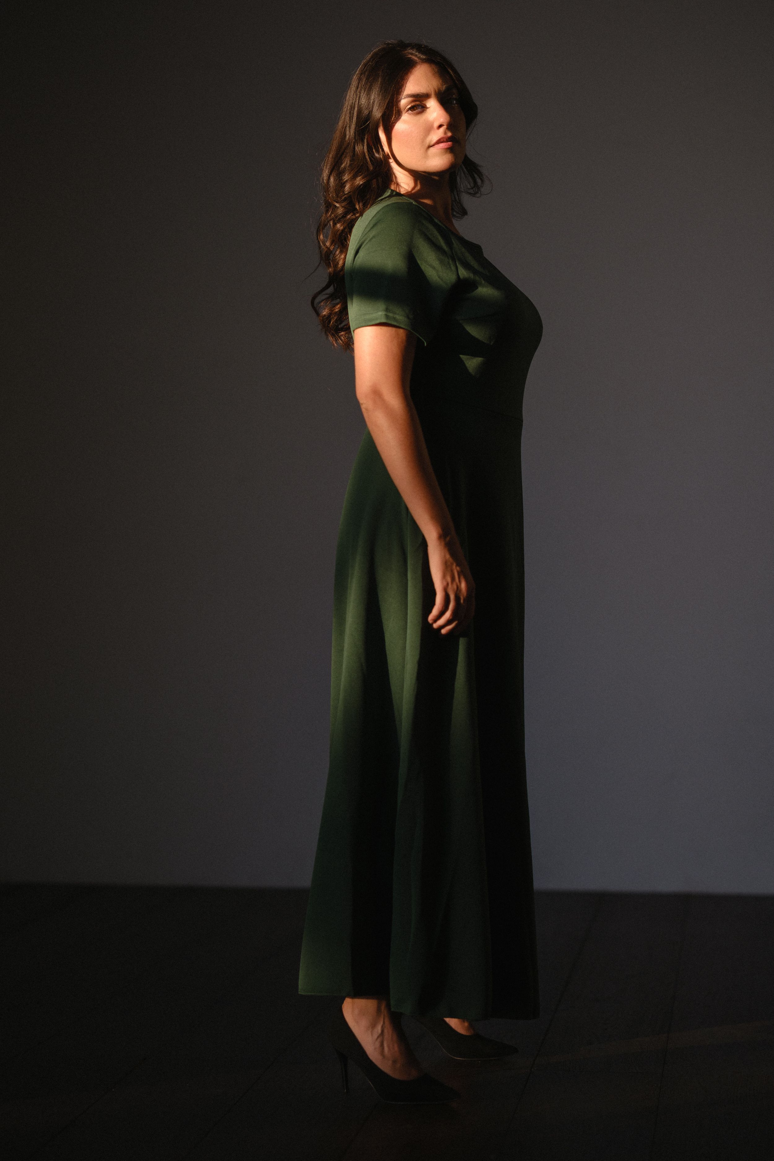 A dark green dress is showcased against a moody black background in a fashion photography series.