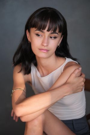 Artistic portrait of a woman in a light tank top against dark background.