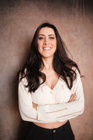 Portrait of a woman in a white cropped sweater and black pants against a textured background.
