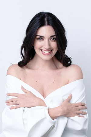 Bright studio portrait of a woman wrapped in a white off-shoulder garment.