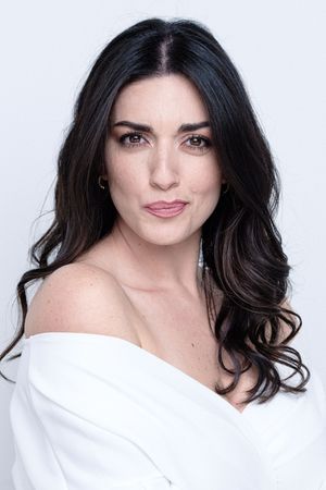 Elegant studio portrait of a woman in an off-shoulder white top against light background.