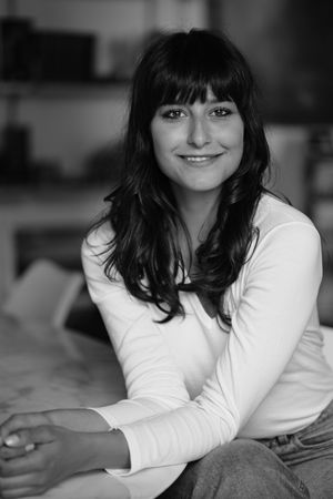 Black and white portrait of a woman with long dark hair and bangs wearing a white long sleeve top.