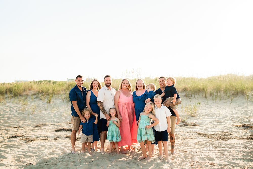 Group of people posing together on sandy beach with sea grass and dunes at sunset.