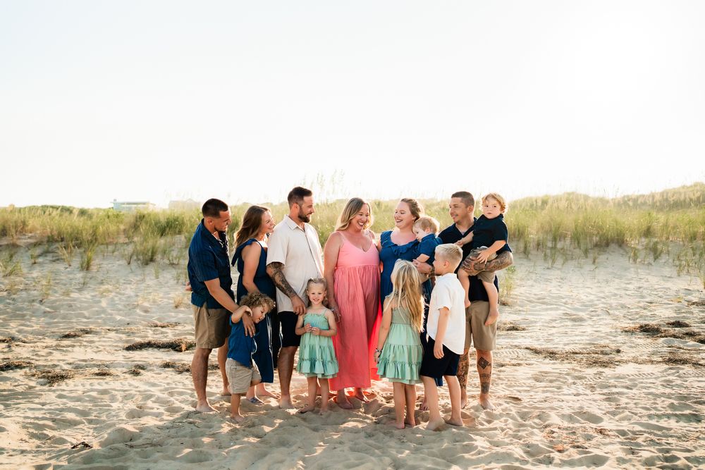 A group walks along a sandy beach shoreline during golden hour, casting long shadows in the soft sunlight.