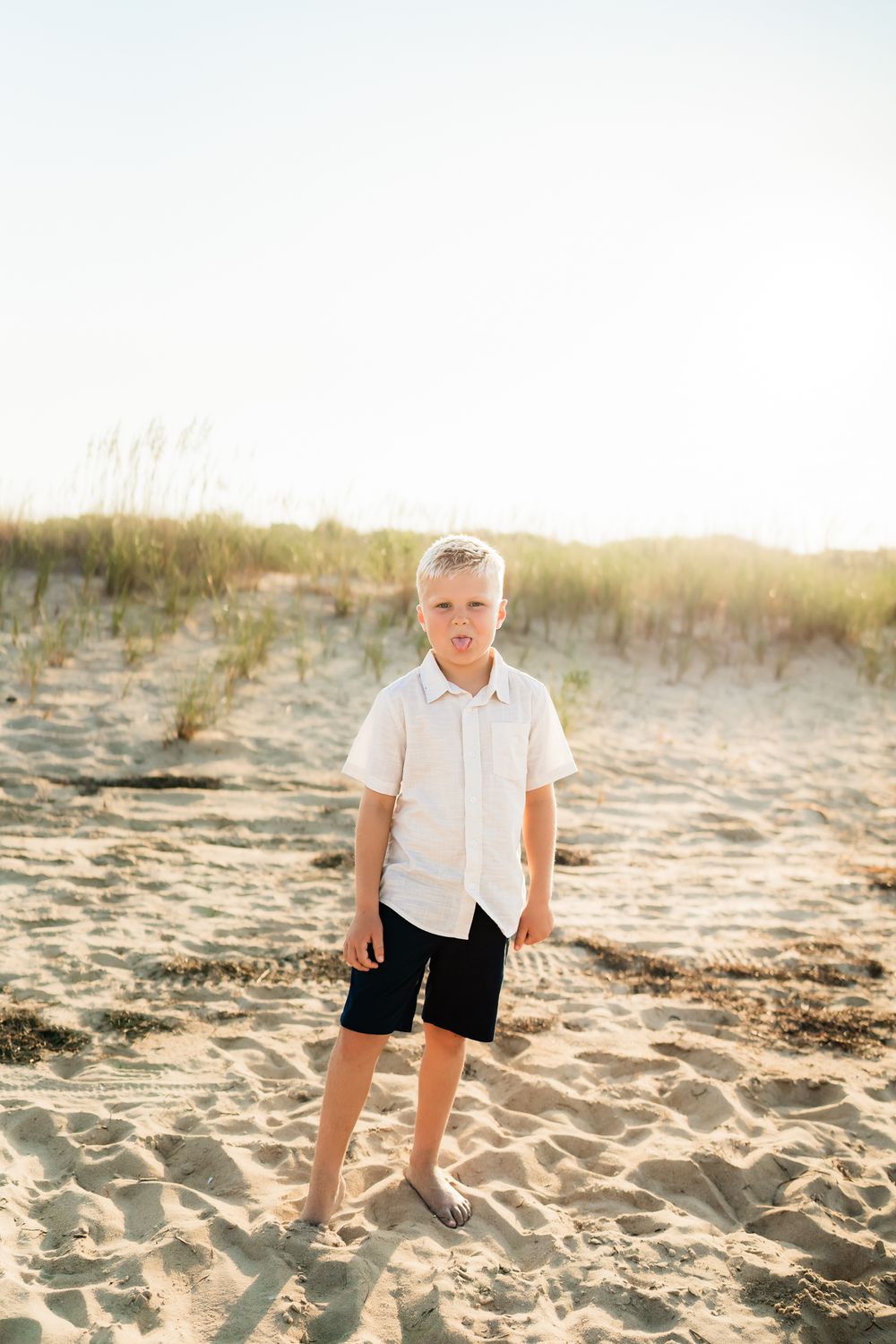 Young child in white shirt and dark shorts playing on a sunny beach during golden hour.