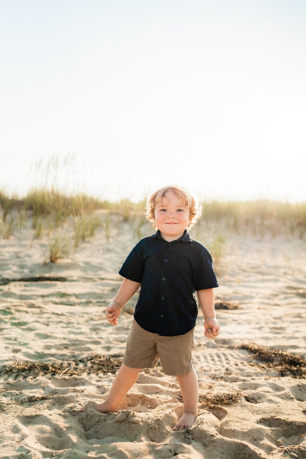 A small child in a black shirt plays in the sand at the beach during golden hour.