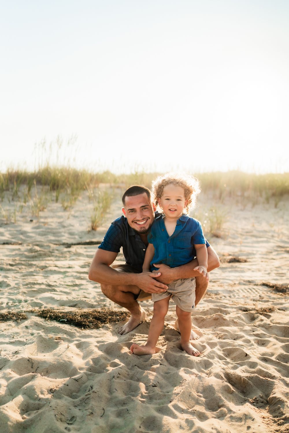 Family playing together in golden sunlight on sandy beach during sunset.